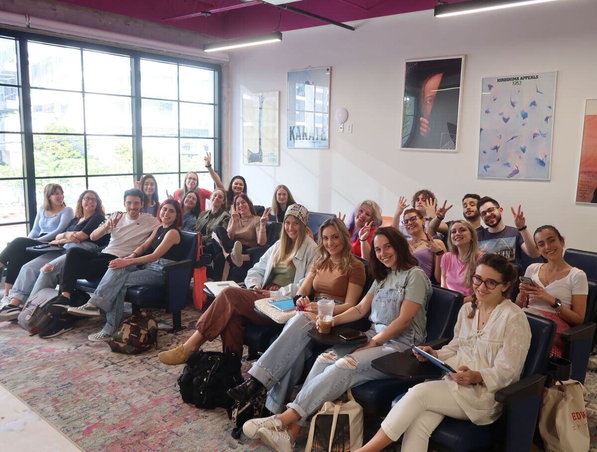 A woman giving a thumbs up to a group of people sitting in a room, showing approval and positivity.